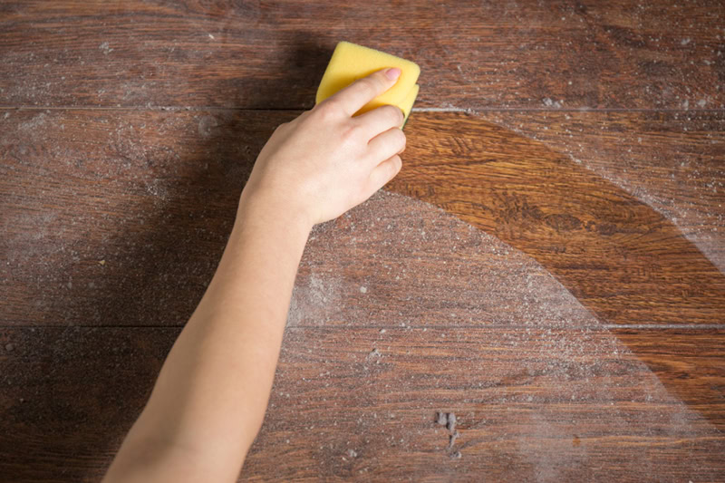 Benefits of Installing an Air Purification System in Your Alpena Home. Photo of someone wiping a table or floor with a yellow sponge.